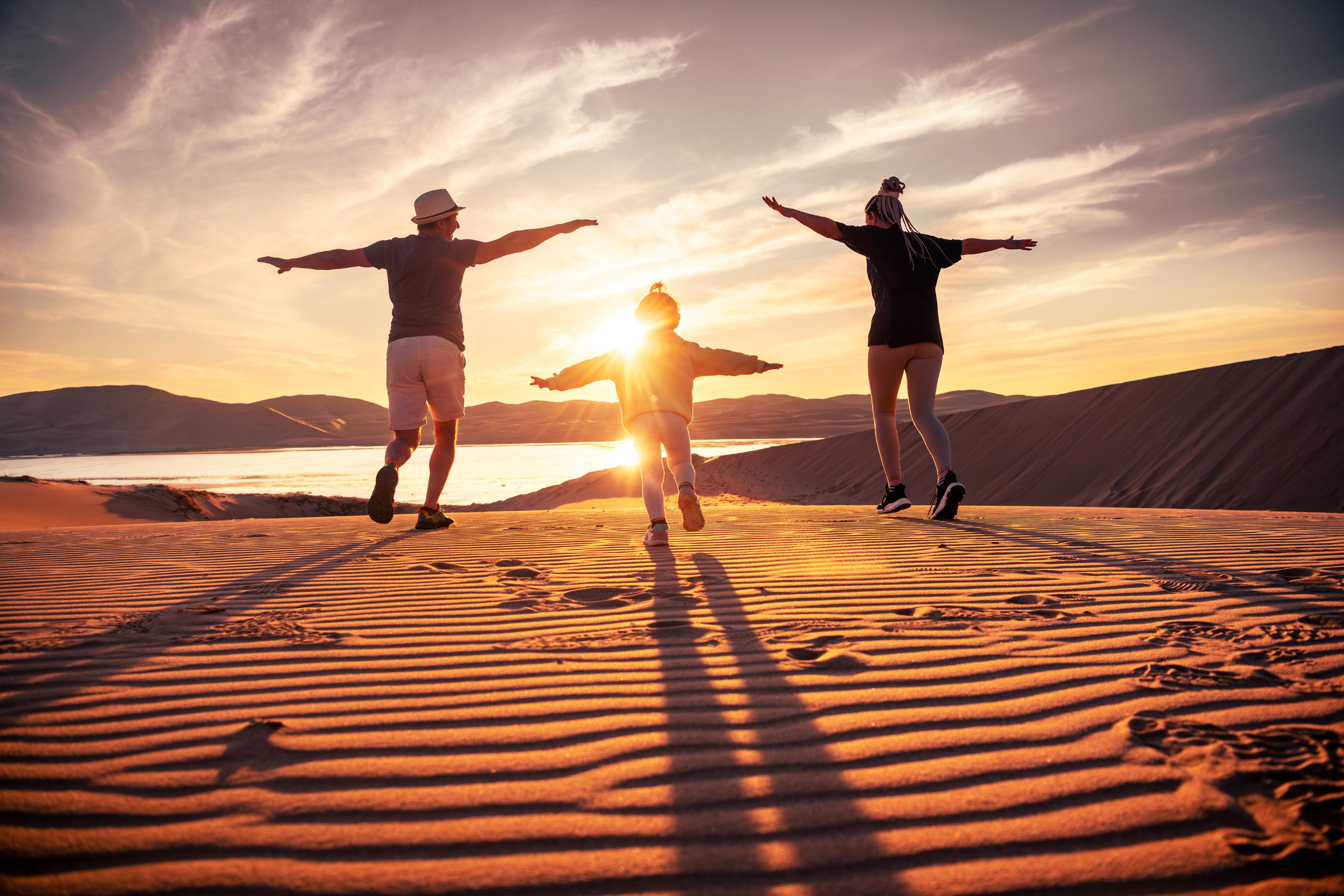 A family jumping on a sand dune at sunset