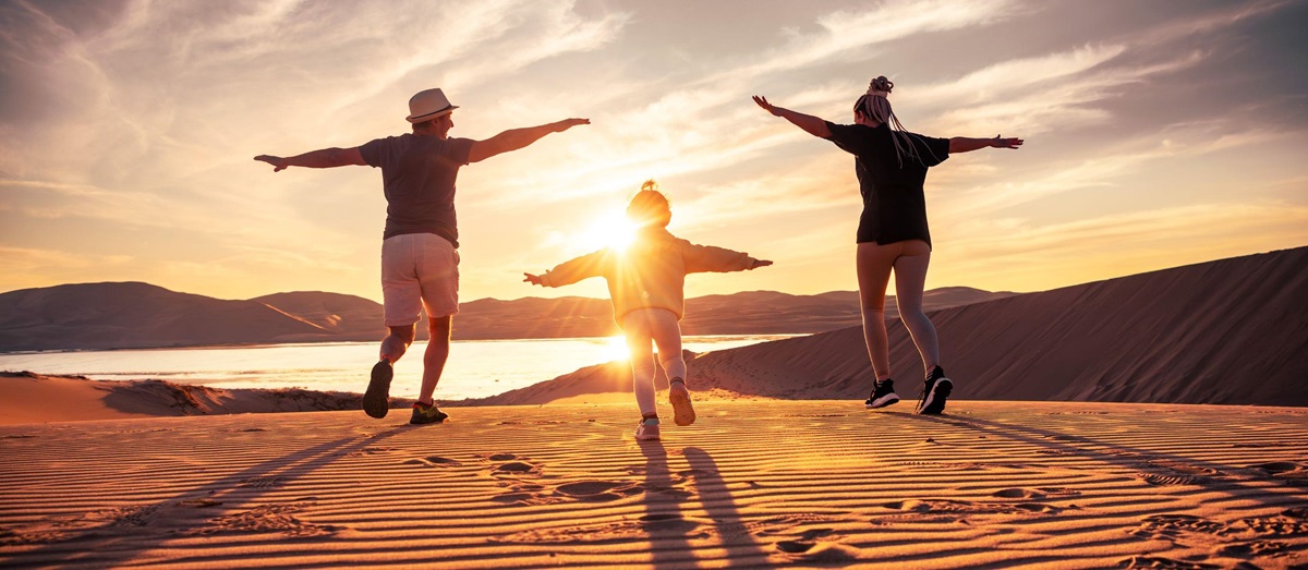 A family jumping on a sand dune at sunset