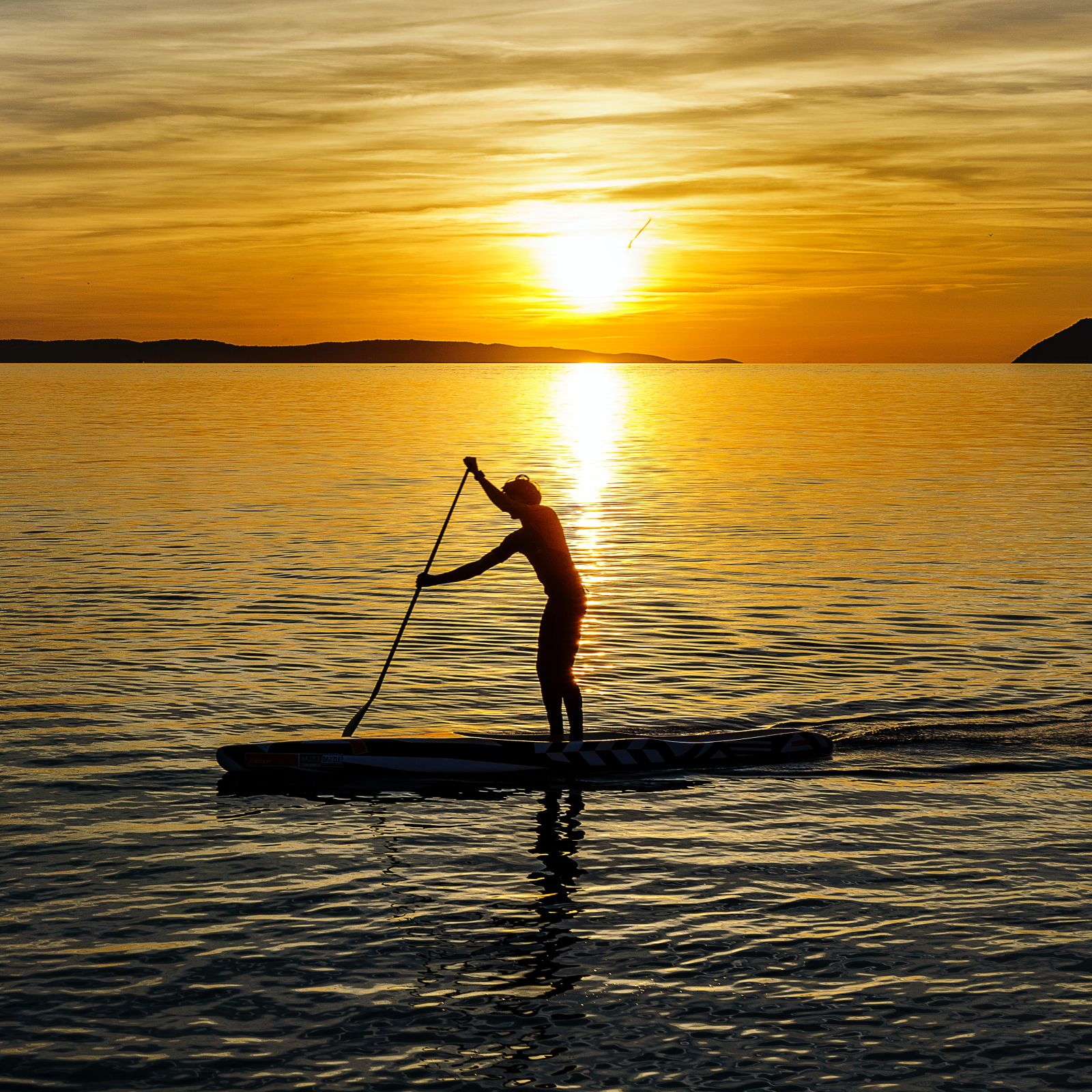 Man stand-up paddle boarding in the sea at sunset