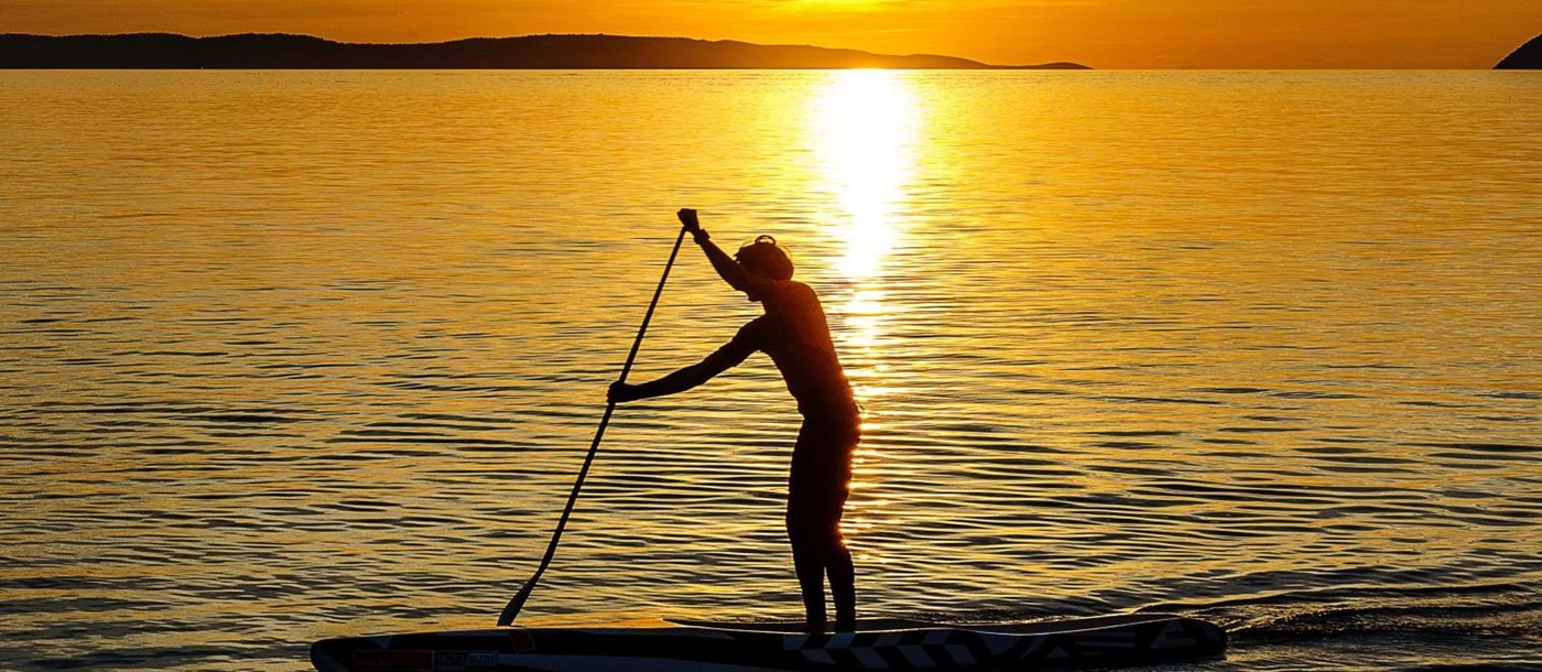 Man stand-up paddle boarding in the sea at sunset