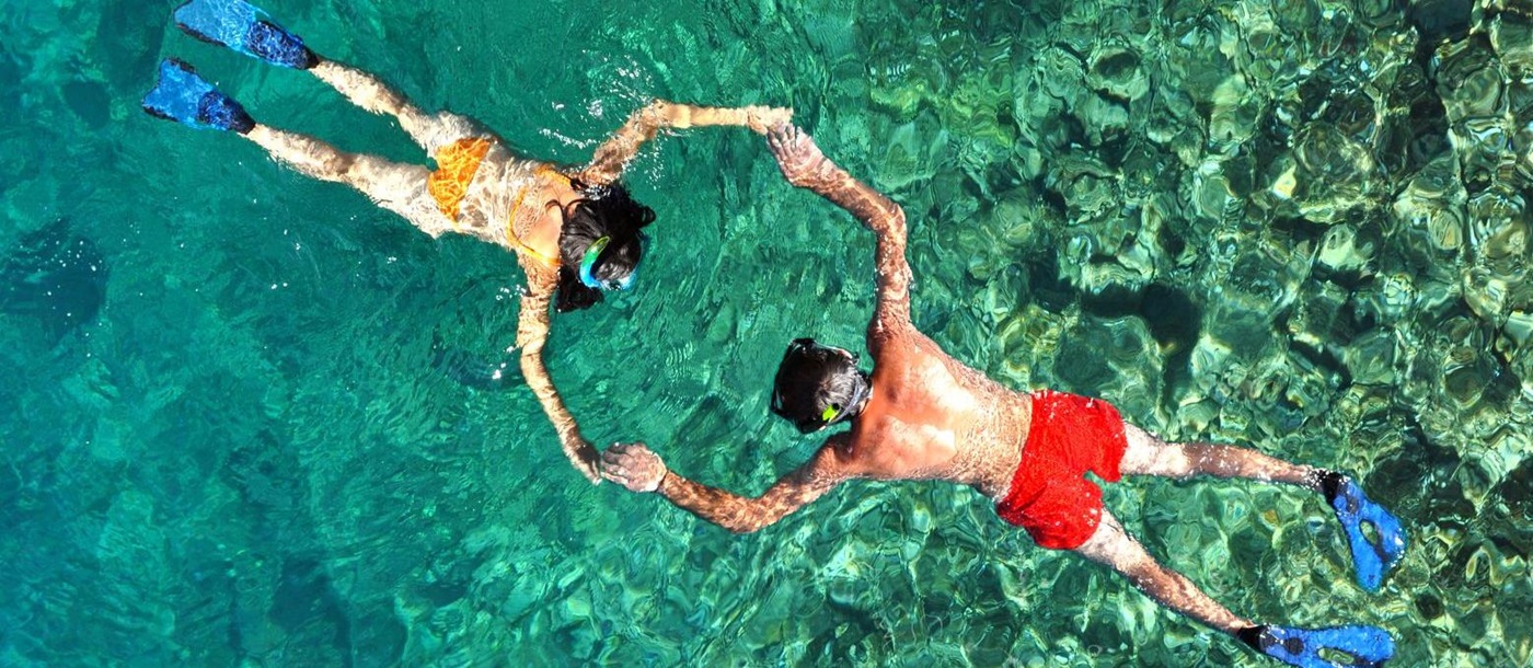 Aerial view of a couple holding hands while snorkelling in crystal-clear waters