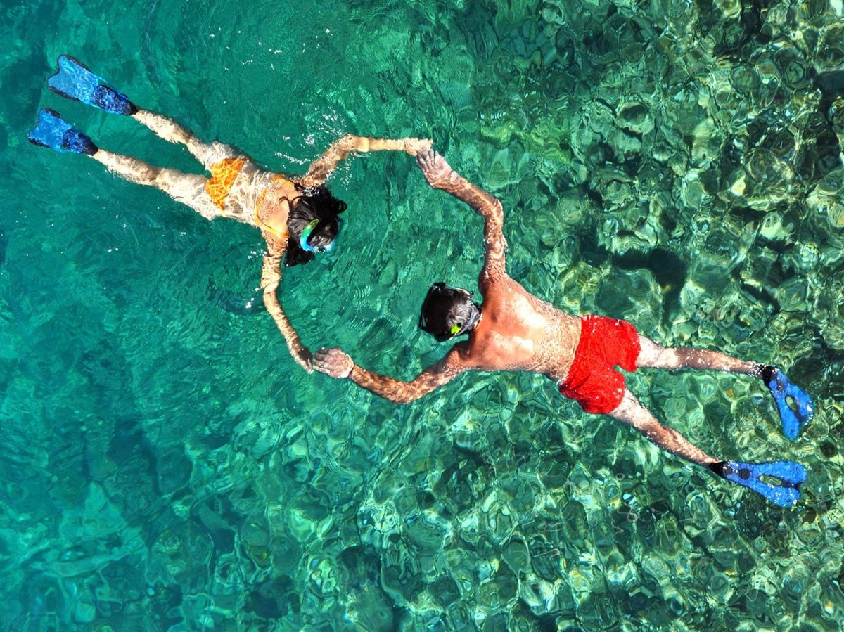 Aerial view of a couple holding hands while snorkelling in crystal-clear waters