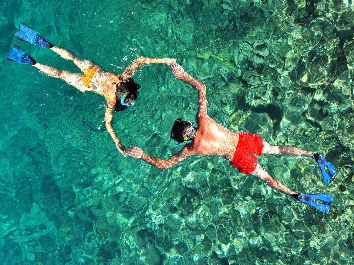 Aerial view of a couple holding hands while snorkelling in crystal-clear waters