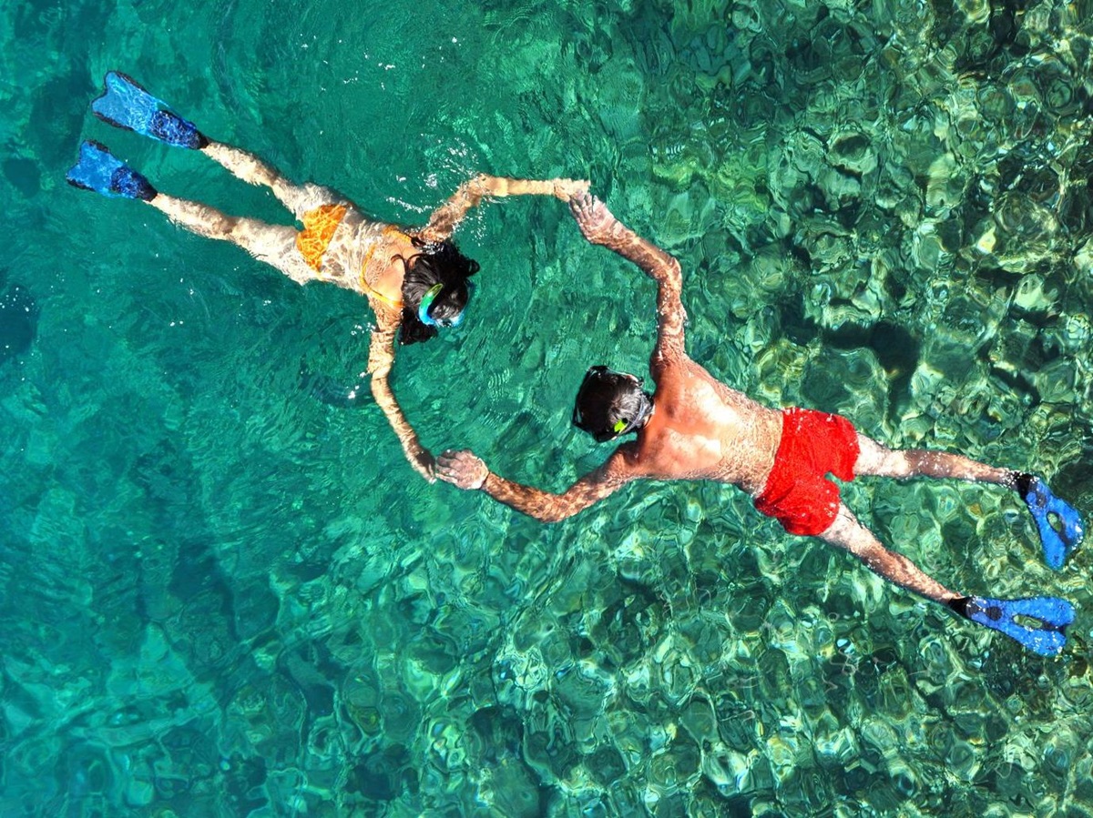 Aerial view of a couple holding hands while snorkelling in crystal-clear waters