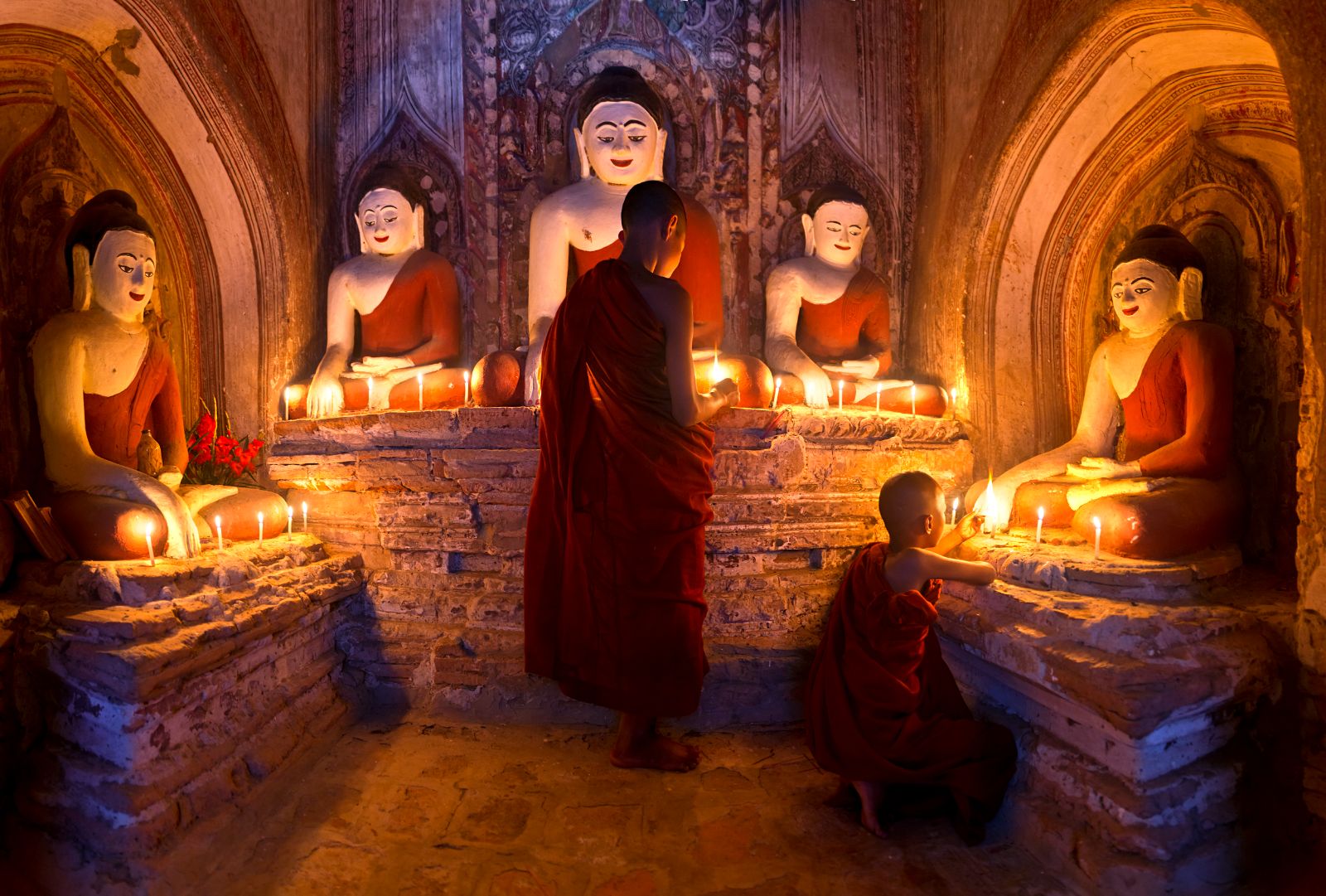 Young Buddhist monks lighting candles in a temple