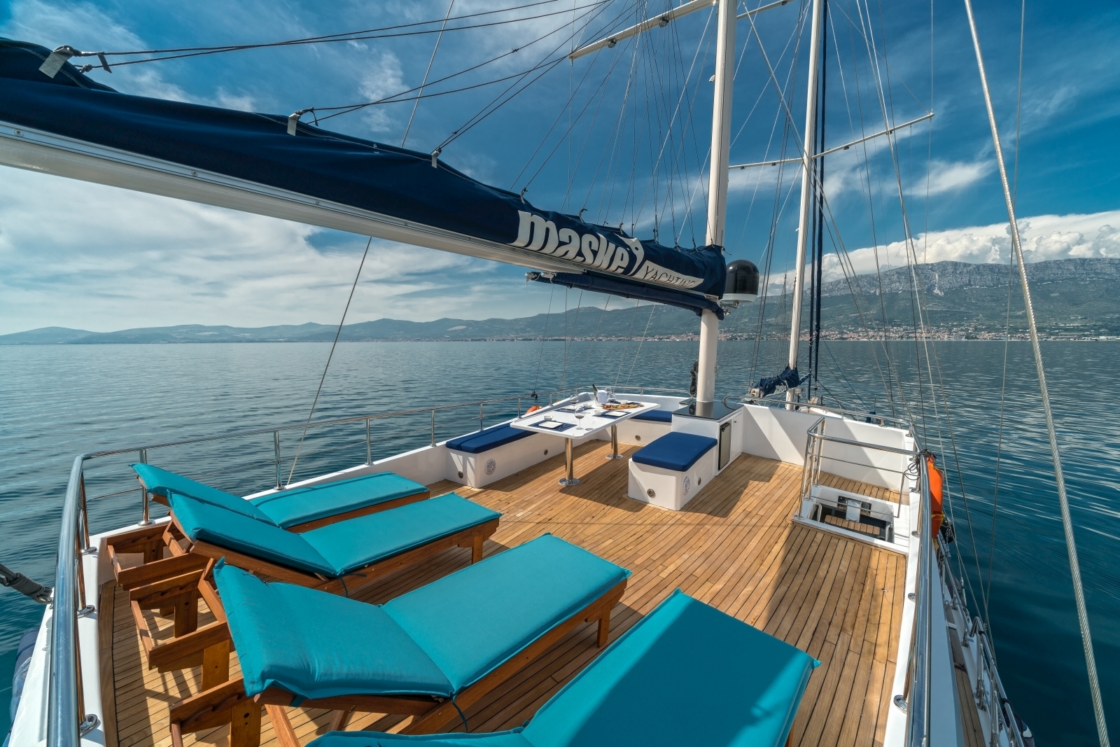 Four wooden loungers with cushions and small seating area on the top deck of the luxury gulet Maske