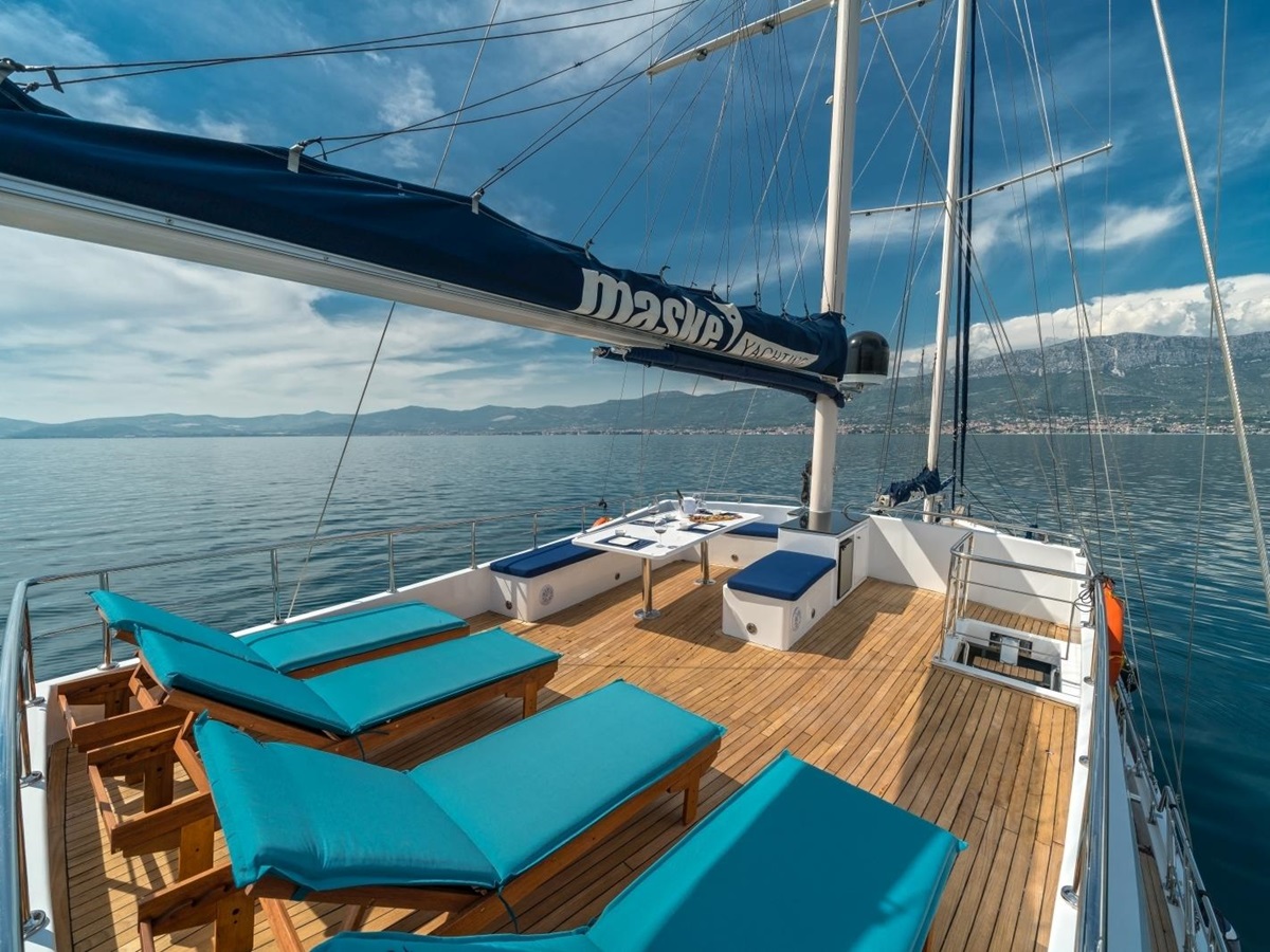 Four wooden loungers with cushions and small seating area on the top deck of the luxury gulet Maske