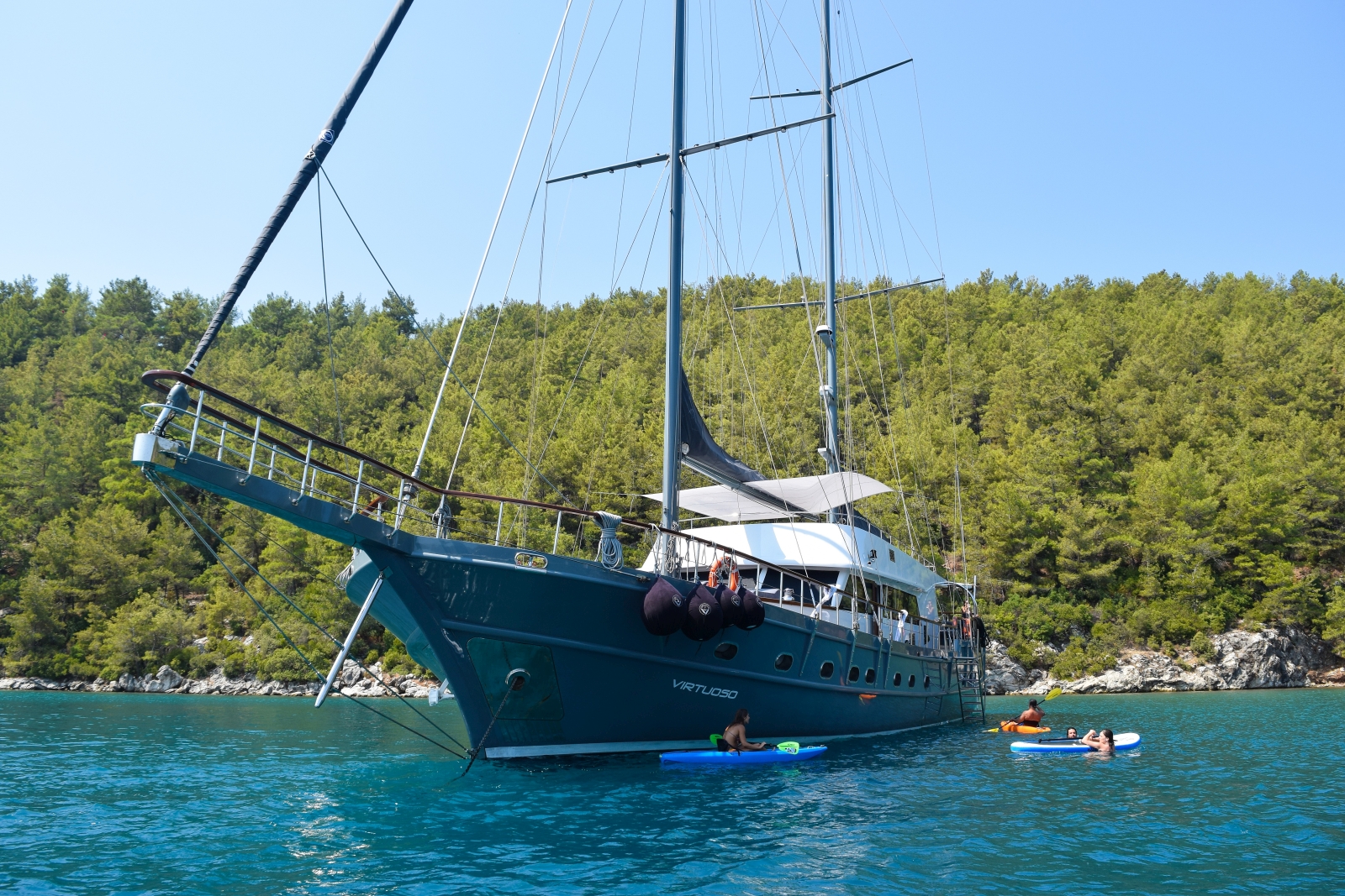 Front view of the luxury gulet Virtuoso with guests playing with kayaks and SUPs in the Greek waters