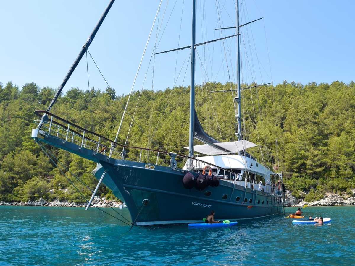 Front view of the luxury gulet Virtuoso with guests playing with kayaks and SUPs in the Greek waters