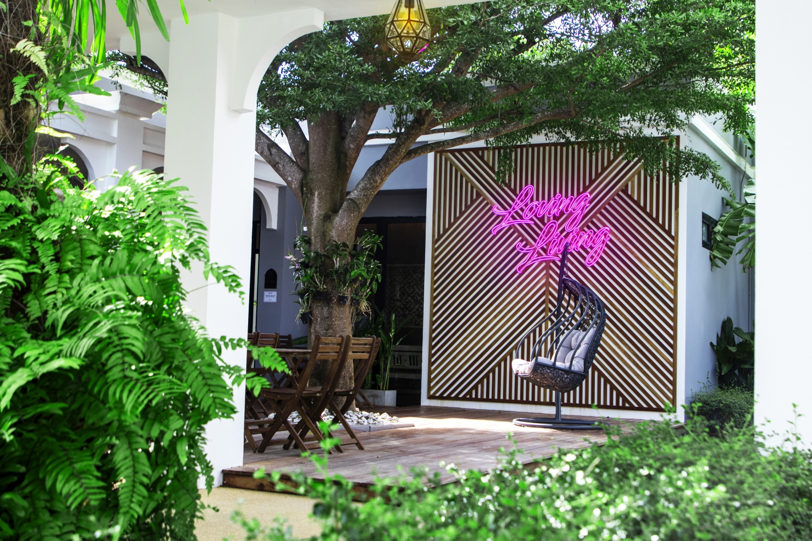 Terrace seating with a hanging egg chair, a feature wall and a neon sign reading "Loving Living" at luxury Zen resort Absolute Sanctuary in Thailand