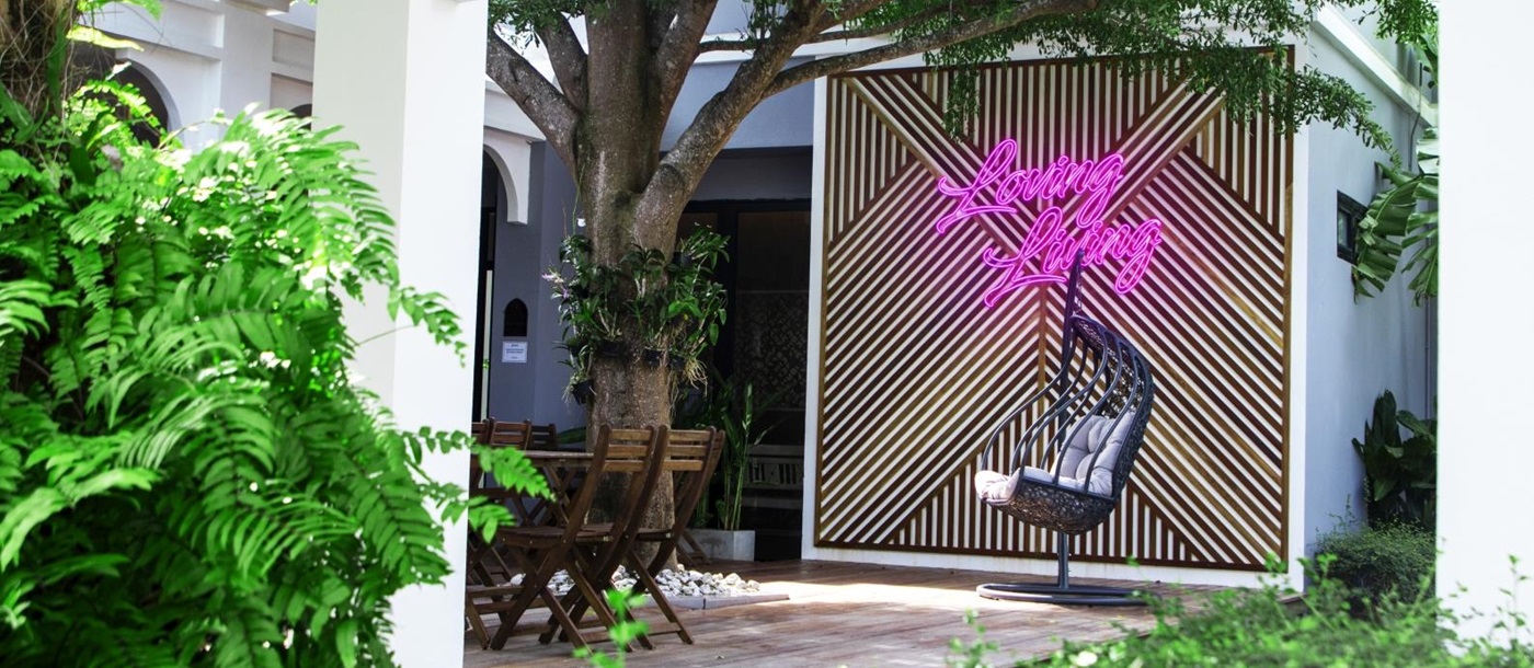 Terrace seating with a hanging egg chair, a feature wall and a neon sign reading "Loving Living" at luxury Zen resort Absolute Sanctuary in Thailand