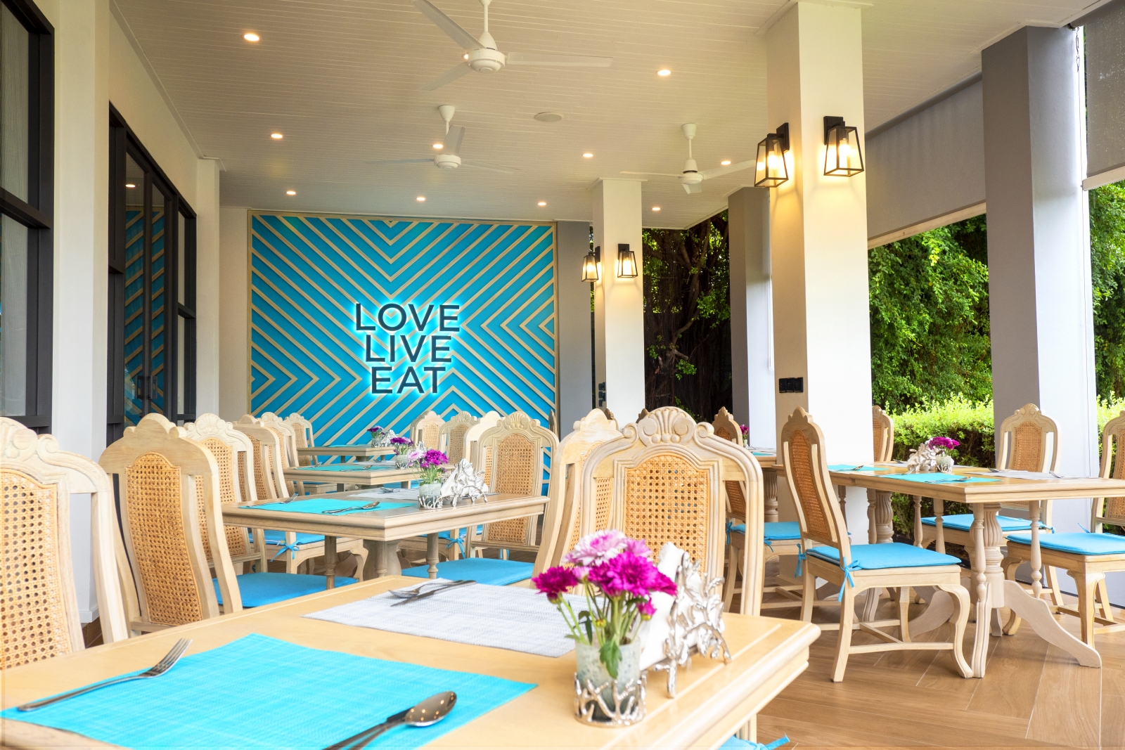 Terrace dining with a blue feature wall and neon sign reading "Love Live Eat" at luxury Zen resort Absolute Sanctuary in Thailand
